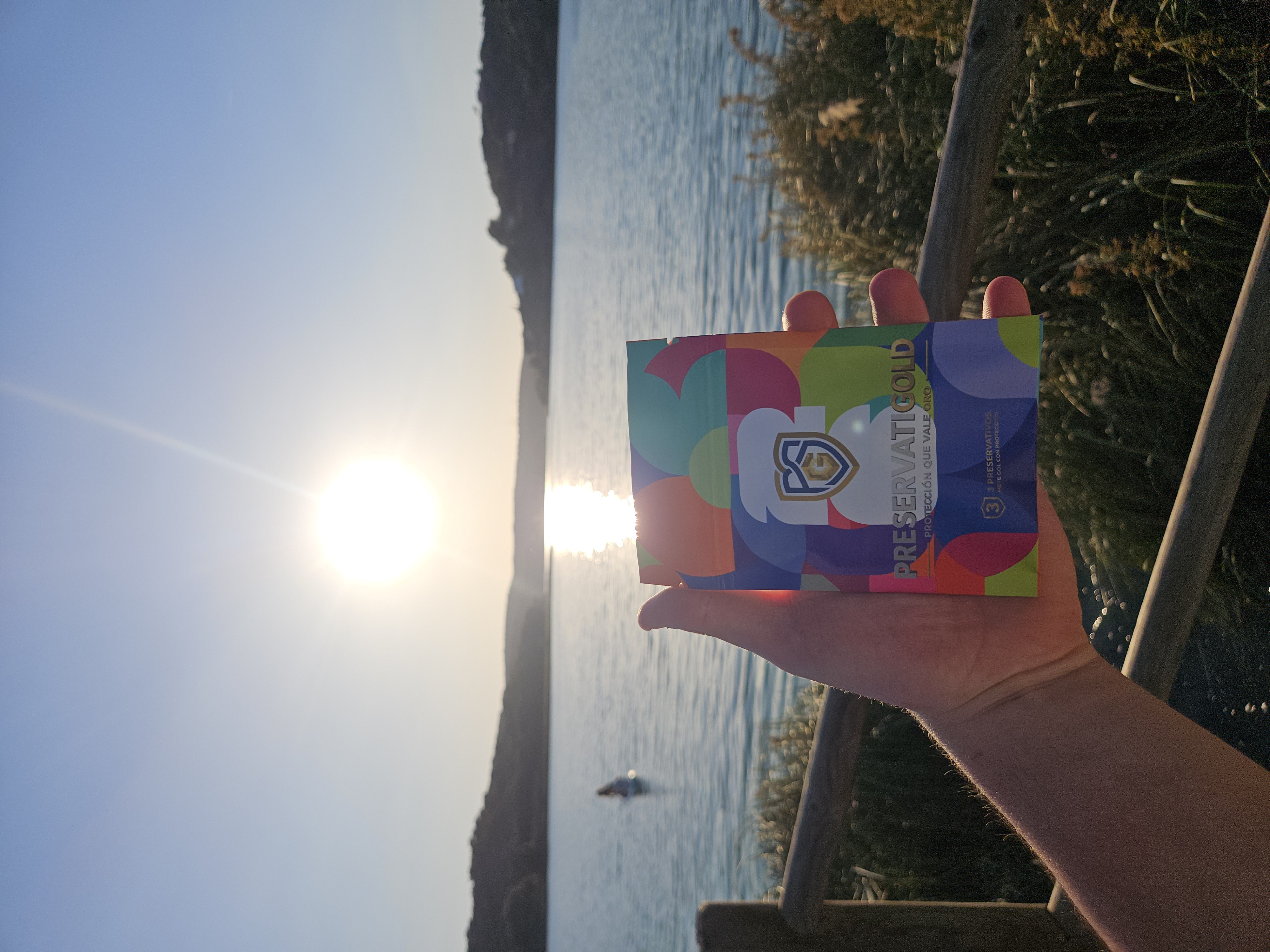 Pack PreservatiGold edición Mundial 2026 sostenido a contraluz del sol brillante sobre el mar, diseño multicolor con el escudo dorado
